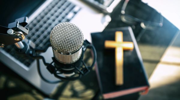 Microphone near a Bible with a cross on top, on a desk with a laptop.