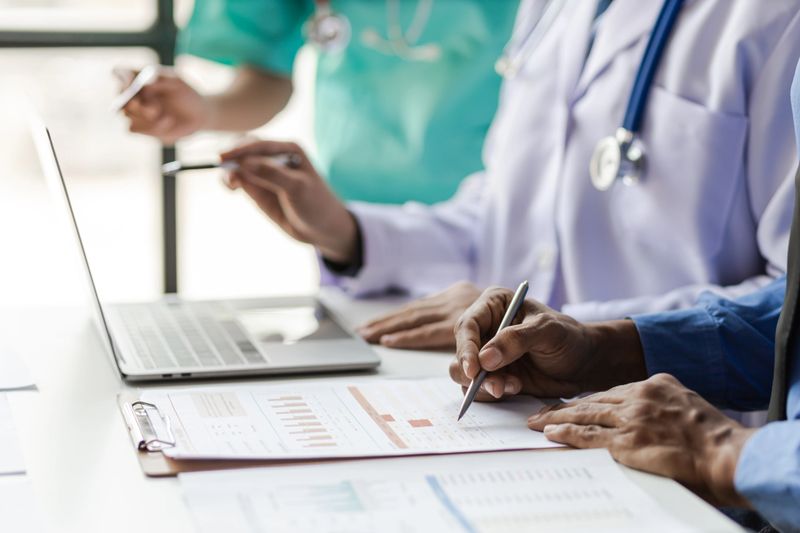 Team, medical analysts and doctors consulting with paperwork of graphs, data and charts in hospital conference room. Healthcare staff discussing statistics, results of research and innovation.