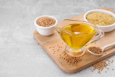 Mustard seeds, mustard powder, and mustard oil in glassware on a wooden board.