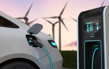 Electric car charging at a station with wind turbines in the background.