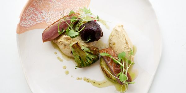 Gourmet dish with duck, grilled vegetables, and microgreens artfully plated.