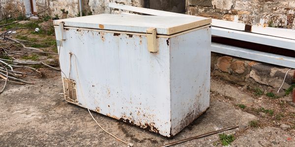 Old, rusty freezer left outdoors on a concrete surface.