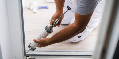 A person applies sealant to a door frame using a caulking gun.