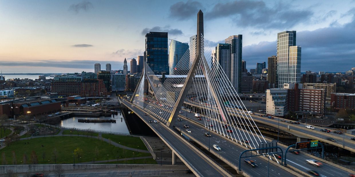 Modern cable-stayed bridge leading into a city skyline at dusk.