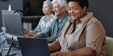 Three seniors working together on laptops in a modern office.