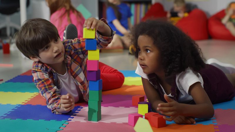 Cute multiethnic preschool kids playing with colored blocks on floor at nursery school. African-American girl and caucasian boy build tower with bricks in kindergarten