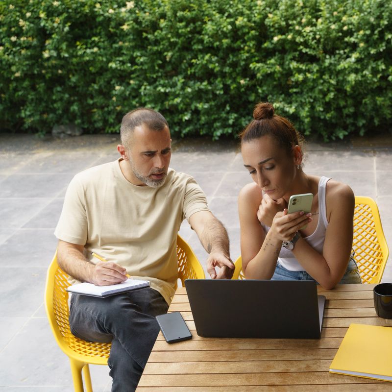 Mid adult co-workers sitting out of the office discussing new projects on laptop