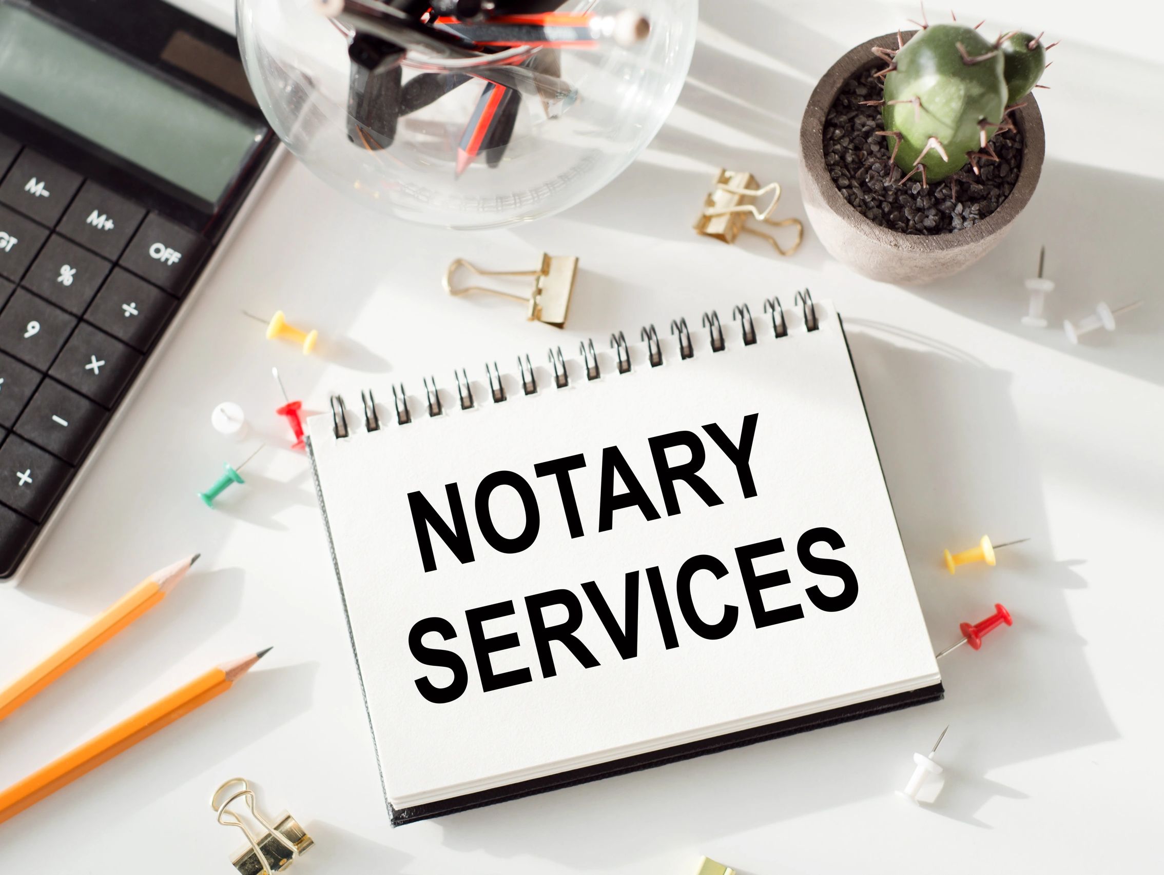Notary services message on a desk with office supplies and cactus.