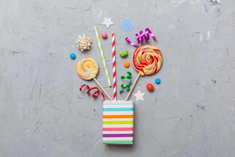 gift box in corner full of assorted traditional candies falling out on colored background with copy space. Happy Holidays sale concept.