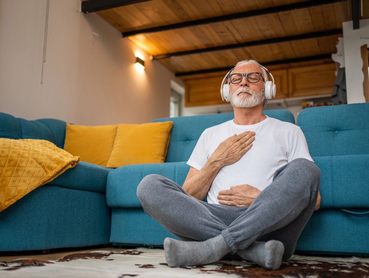 Man seated on the floor, with hands placed over heart and belly. Eyes closed and wearing headphones