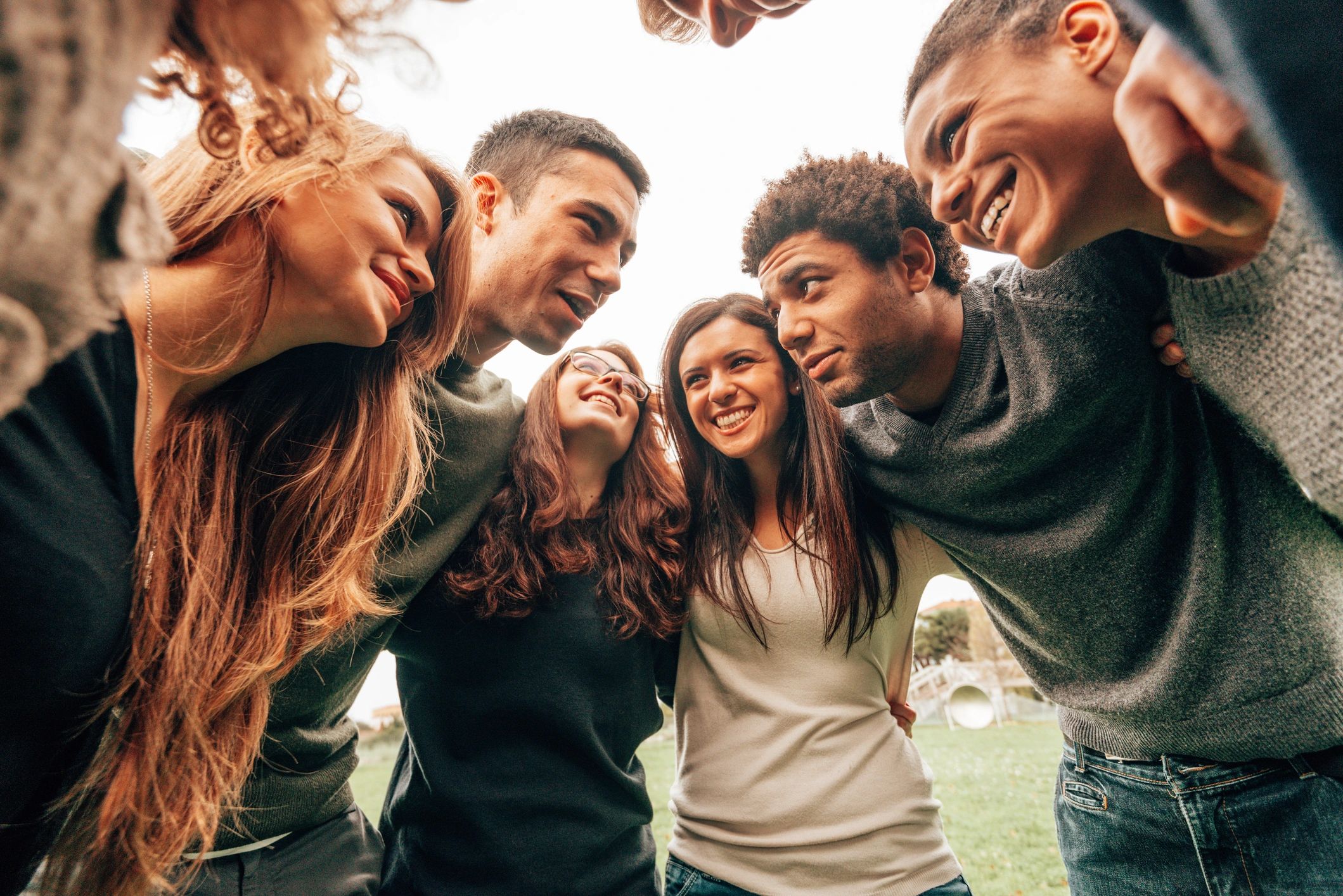 Group of friends huddled in a circle, smiling and enjoying each other's company outdoors.