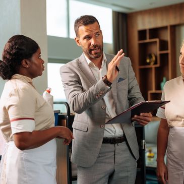 Manager giving instructions to two housekeepers in a hotel setting.