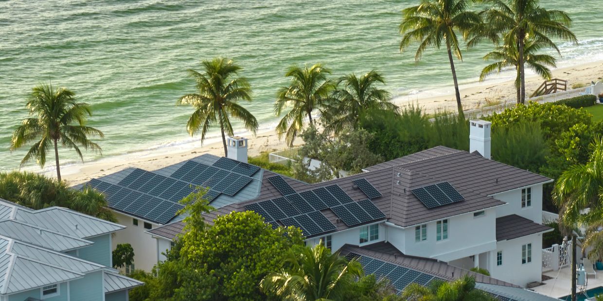 Coastal homes with solar panels and palm trees by the beach.