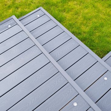 Close-up of a modern gray wooden deck against green grass.