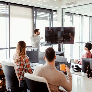 A man presenting code to colleagues in a modern office meeting room.