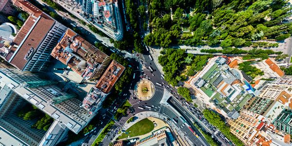 Aerial view of a city with a roundabout, buildings, and a large green park area.