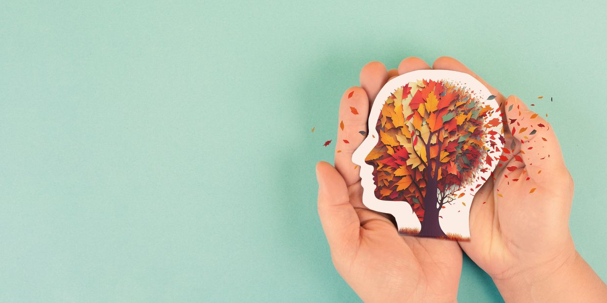 Hands holding a head silhouette with a tree and falling autumn leaves inside.