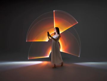 Woman in white dress using phone with glowing abstract light art behind her.