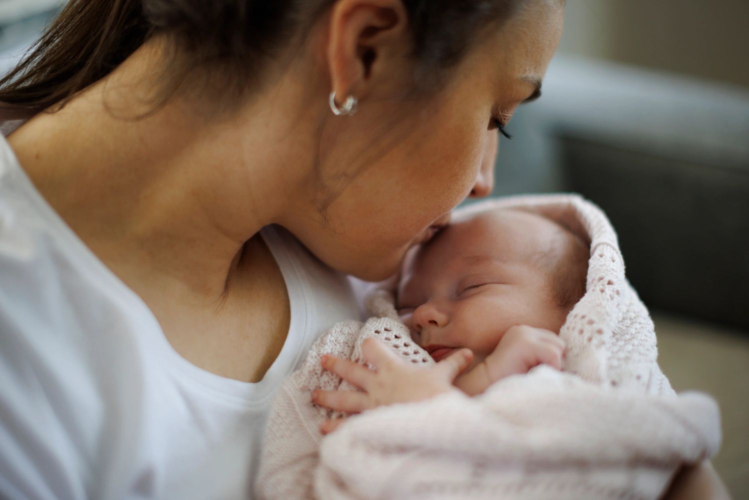 A mother gently kisses her sleeping newborn, capturing an intimate postpartum moment of closeness and care.