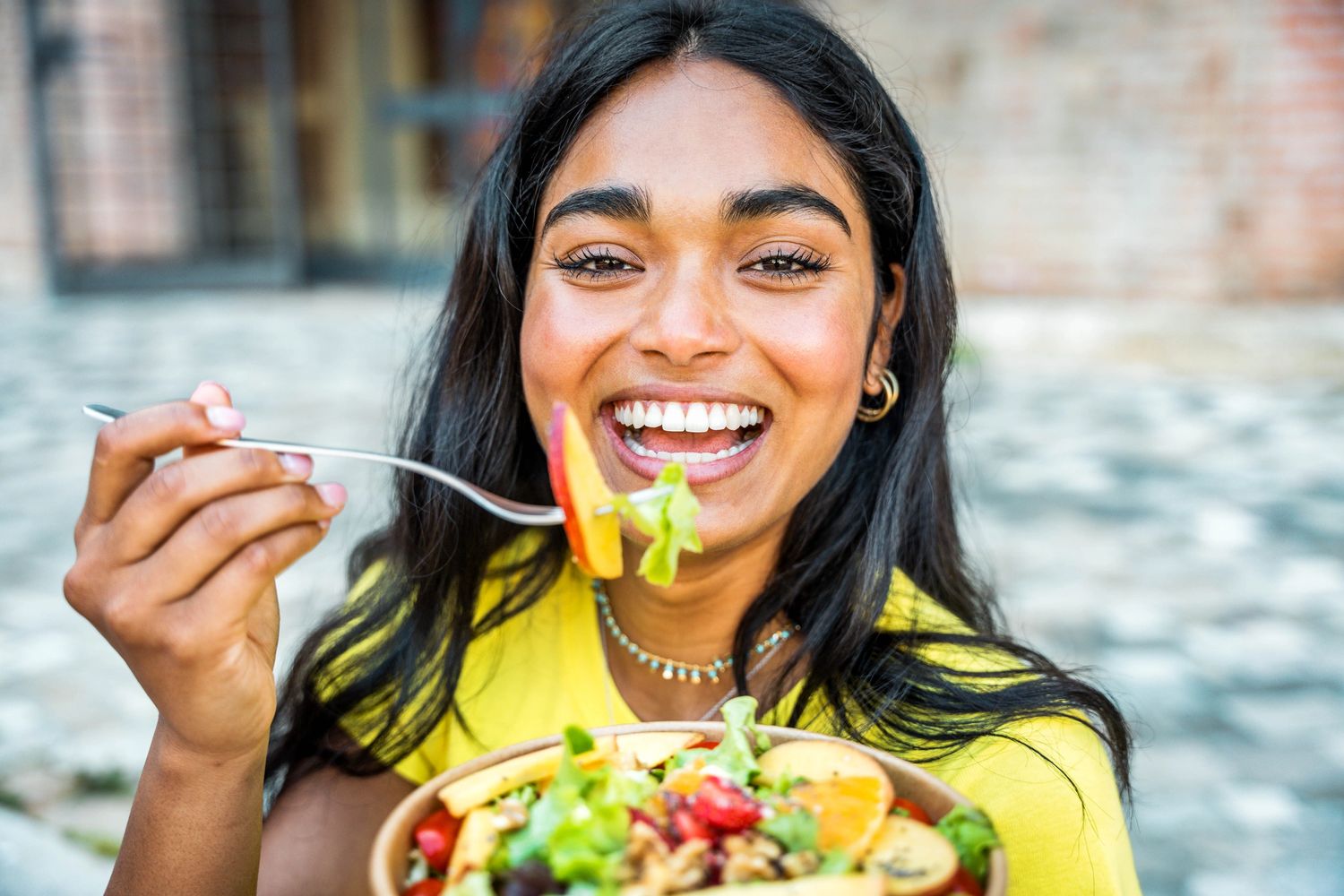Healthy, fit woman s,iling while eating a vibrant colored salad