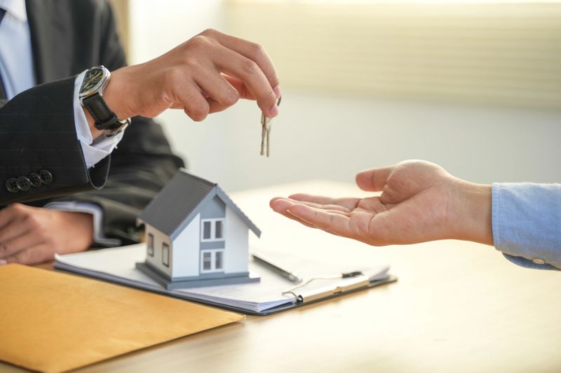 A real estate agent gives a client the house keys after signing a real estate contract with an approved mortgage form. About offering mortgage loans and home insurance.