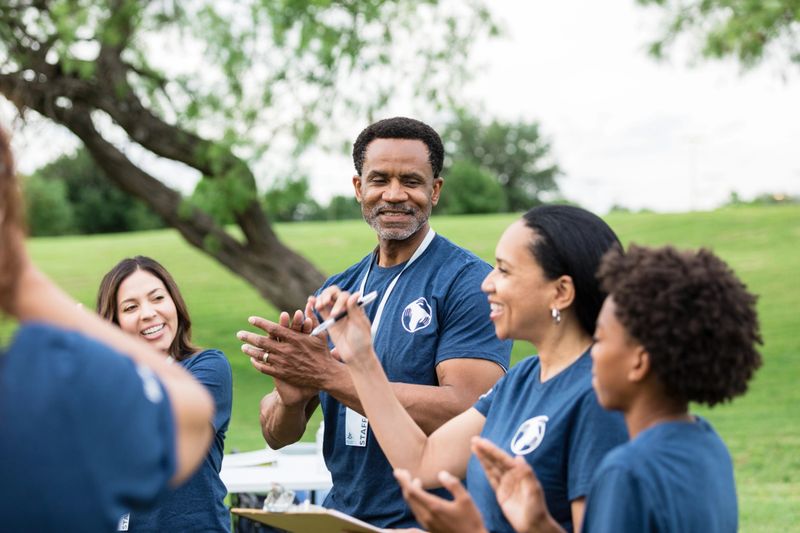 At the volunteer park day, the multiracial group of volunteers smile and clap for the mature adult female coordinator.