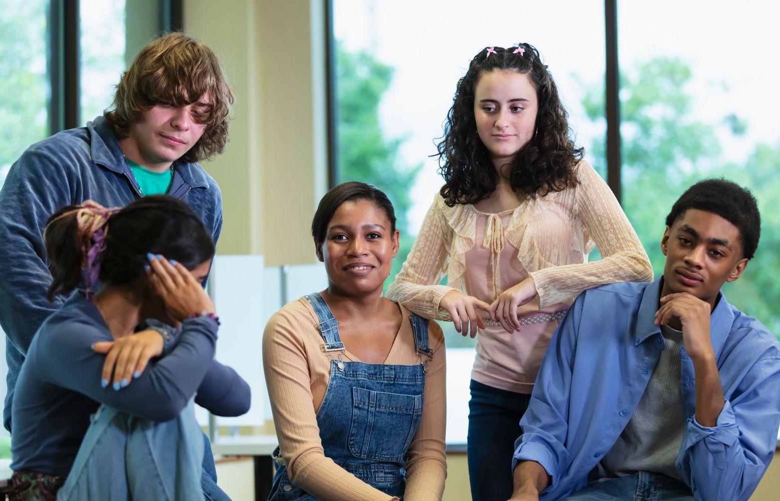 A group of diverse young people with mixed emotions, one looking upset.