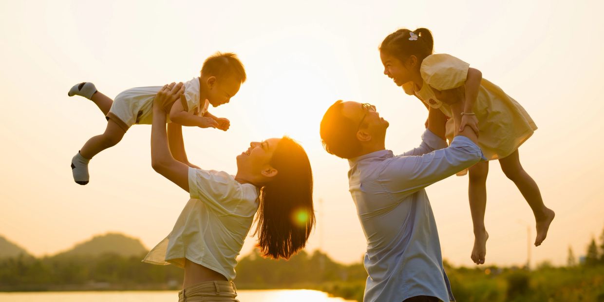 Parents joyfully lift their children against a sunset backdrop outdoors.