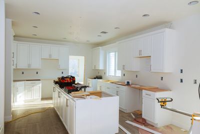 Kitchen under construction with white cabinets and tools on the island.