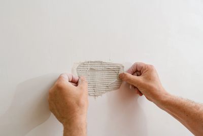 Hands repairing a hole in a white wall.