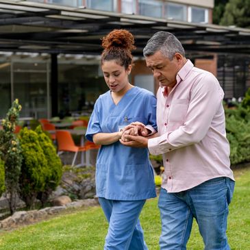 Latin American senior man walking outdoors at the hospital holding hands with his caregiver
