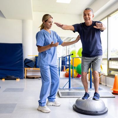 Therapist assisting elderly man with balance exercise on a BOSU ball.