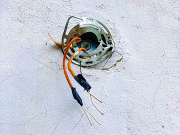 Exposed electrical wires protruding from a wall socket.
