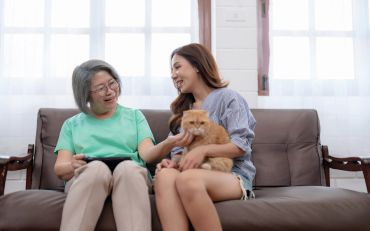 Two women sitting on a couch with a cat.