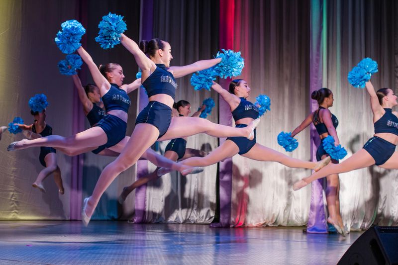 athletes perform on stage, young cheerleaders perform at the cheerleading championship, girls in a jump, girls are holding pompons, hands raised up, girl doing acrobatic and flexible tricks
