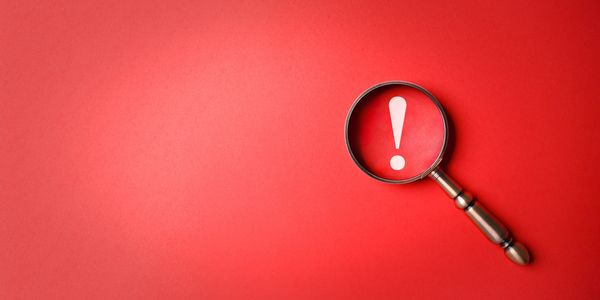 Magnifying glass highlighting a white exclamation mark on a red background.