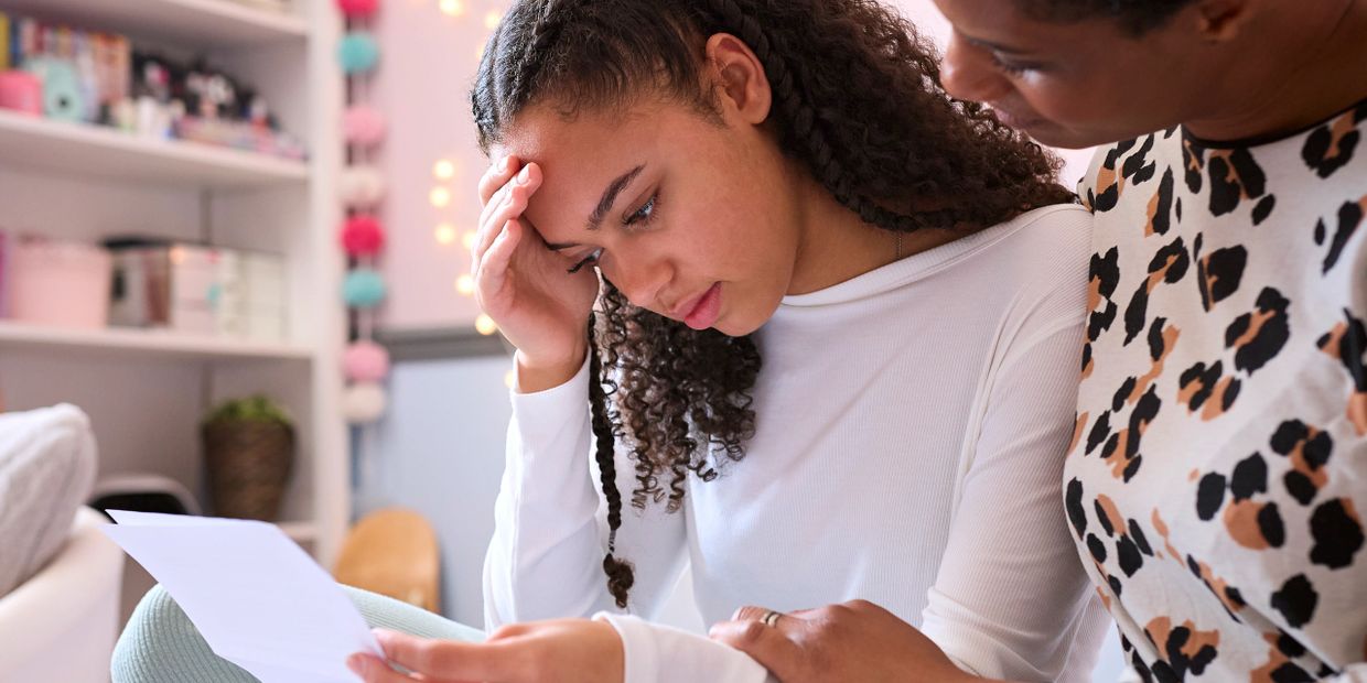 A young woman looks worried while reading a document, comforted by another person.