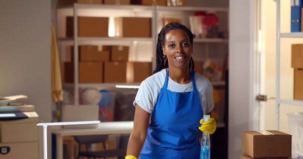 Smiling woman in blue apron and yellow gloves holding a spray bottle , cleaning for a cleaning company in curacao