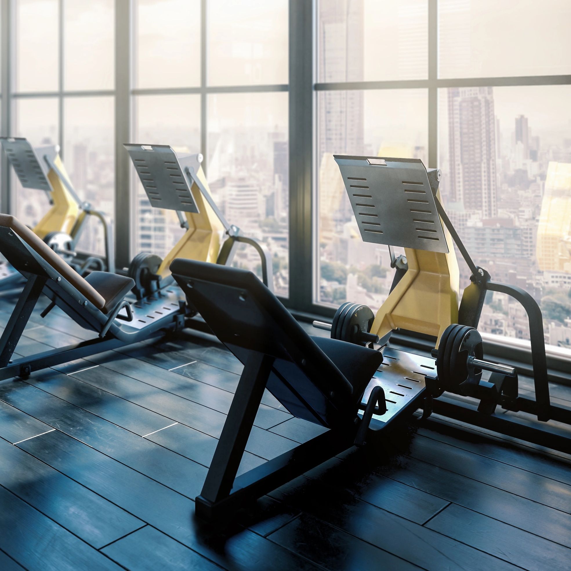 Modern gym with leg press machines and large windows overlooking a cityscape.