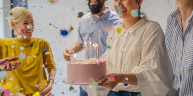 Group celebrating with a pink cake and candles.