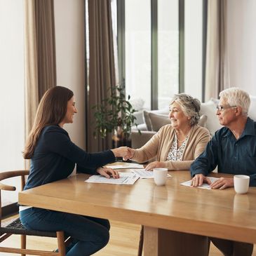A young woman shakes hands with an elderly couple at a table with documents.