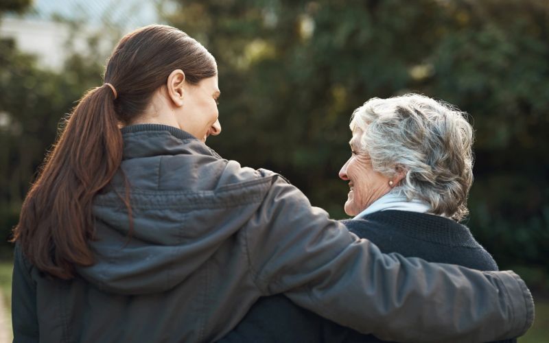 Back, mother and adult daughter outdoor, hug and happiness with quality time, bonding and loving together. Senior woman, female people and family embrace, park and conversation with support and love