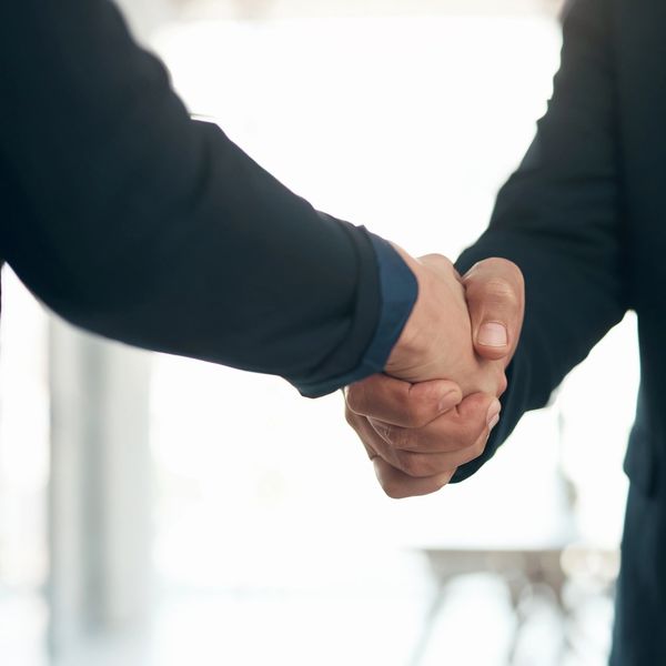 Two people in suits shaking hands in a bright room.