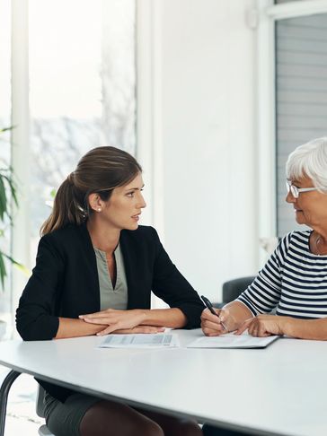 Two women engaged in a serious discussion over documents at a bright office table.