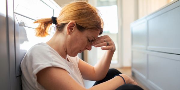 Woman sitting on floor, holding her forehead, looking stressed.