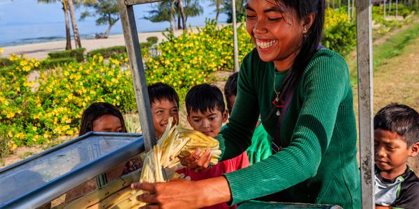 A woman smiles while preparing sugarcane juice with children watching.