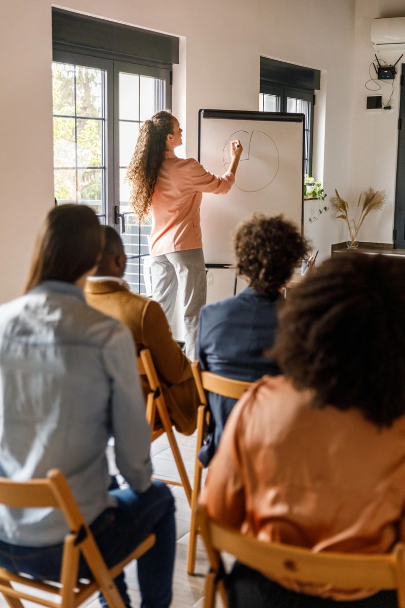 Selective focus shot of young businesswoman writing data on a whiteboard while holding a presentation for a group of diverse, engaging business people.