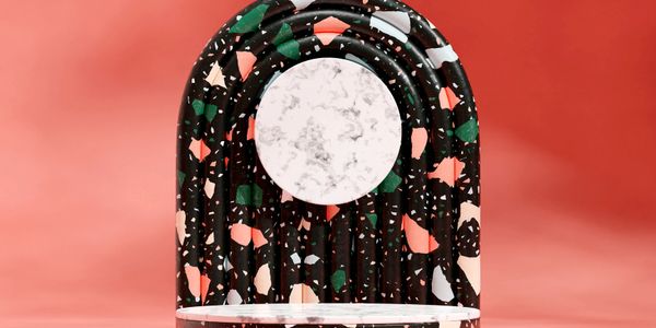 Colorful terrazzo arch with a round marble mirror on a coral background.