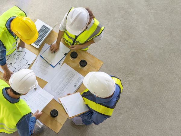 Four construction workers review blueprints and notes at a table.