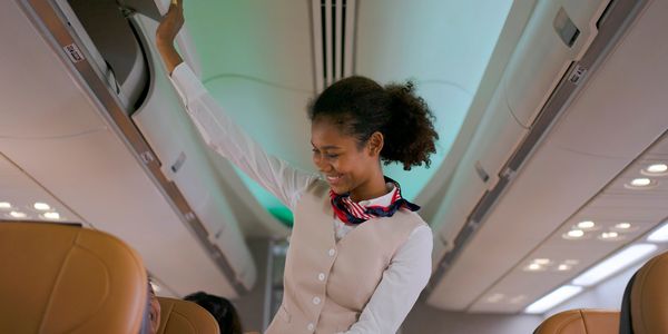 Flight attendant smiling while assisting a passenger with overhead luggage.